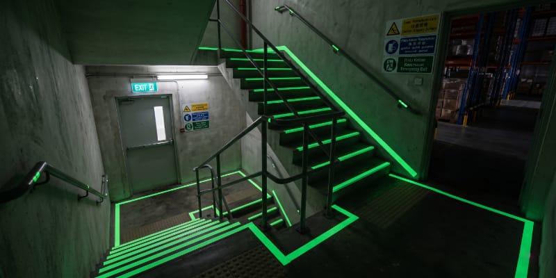 Industrial warehouse emergency stairway equipped with glow in the dark anti-slip stair nosing and luminous floor markings, OSHA-style safety environment