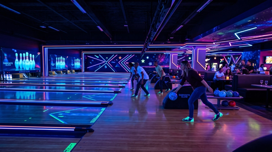 Modern bowling centre with polished bowling lanes and subtle photoluminescent glowing accents along lane surrounds and architectural edges, cosmic atmosphere, realistic UV lighting
